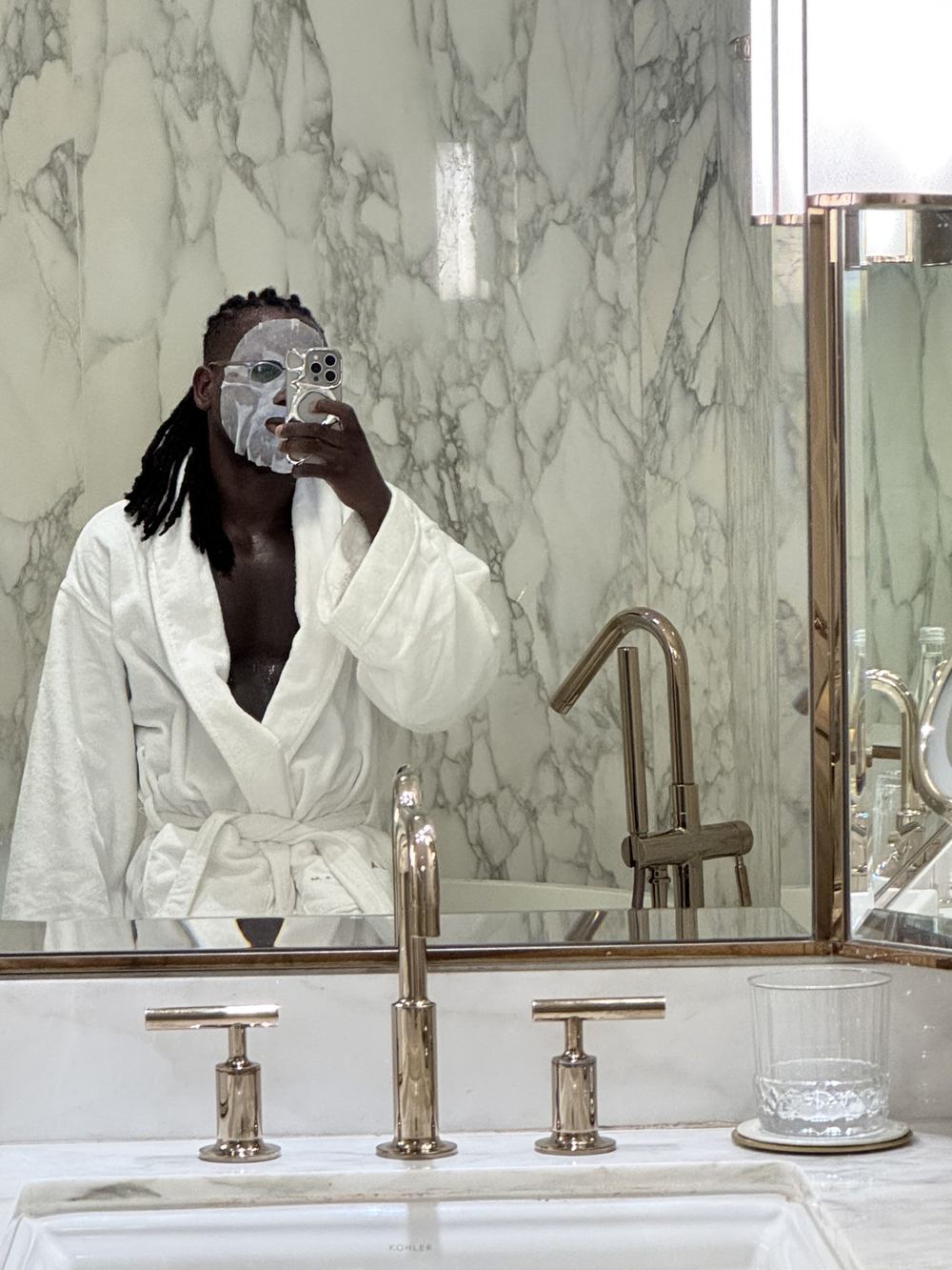 Zach in a hotel robe and sheet mask taking a mirror selfie at The Langham Jakarta